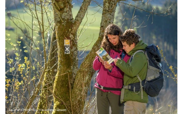 Zwei Wanderer schauen in den Erlebniswanderführer Sauerland-Höhenflug